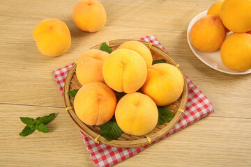 Fresh Yellow Peaches in Wicker Basket on Wooden Table with Red Checkered Cloth