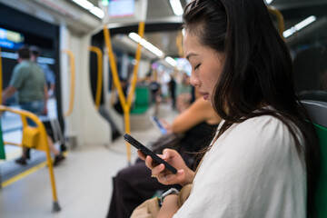 Asian woman commuting on Malaga metro with smartphone