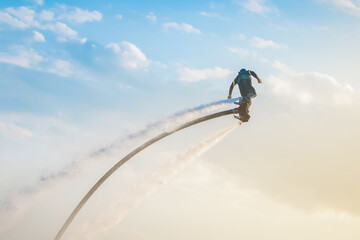 Flyboarding adventure in clear skies over the ocean during sunset with a rider soaring high. Flyboarding athlete with jet stream flying on a flyboard against the sky extreme sports