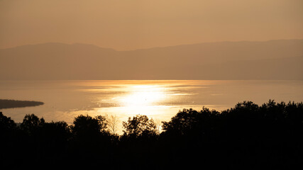 Coucher de soleil sur le lac Léman or brillant depuis la rive française avec vue sur sur la silhouette de la rive suisse. 