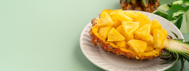 Fresh pineapple chunks served in a pineapple bowl on green table background.