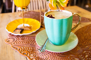 A cup of latte with a small flower in a turquoise cup