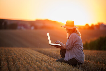Woman agronomist analyzing smart farming data on laptop after harvest on agricultural field during sunset