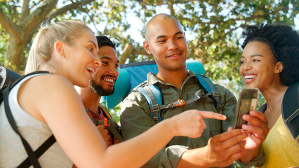 Group Of Friends With Backpacks Using GPS On Mobile Phone On Vacation Hiking In Countryside