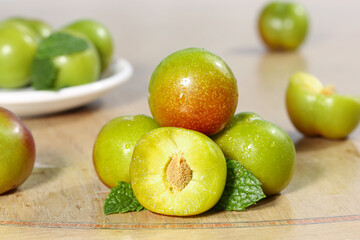 Fresh Green Plums on Wood Base with Half Cut Fruit Showing Pit and Mint Leaves