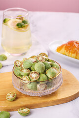 Fresh Kumquats in Crystal Bowl with Herbal Tea and Pastries on Pink Background