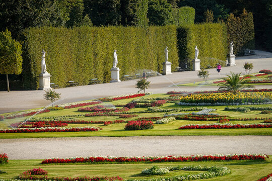 View of vibrant flower beds and statues lining the manicured gardens under the summer sun, a jogger enjoying the scenery, Sch&Atilde;&para;nbrunn Palace, Wien, Austria.