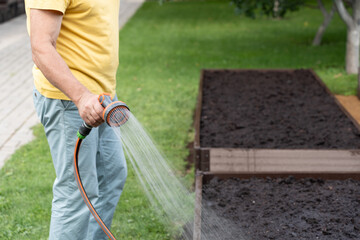 Senior man watering garden with hose in backyard. Organic farming and gardening concept,...