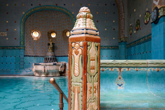 View of ornate tilework shimmers around a turquoise thermal pool, reflecting the soft glow of distant windows, in Gell&Atilde;&copy;rt Thermal Bath, Budapest, Hungary.