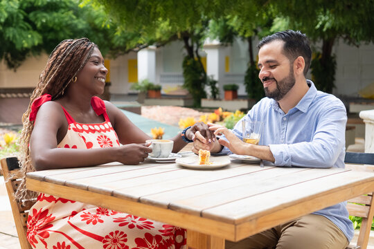Happy interracial couple holding hands and drinking coffee at outdoor cafe