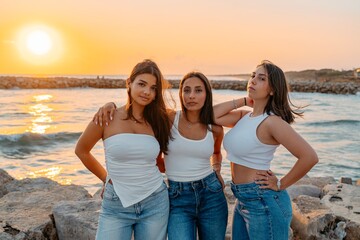 Stylish Trio of Young Women Posing by the Sea at Sunset