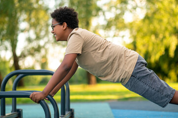 Fototapeta premium Curly-haired teen exercising at the playground and looking excited