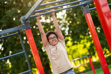 Fototapeta premium Curly-haired boy doing exercises at the playground in the morning
