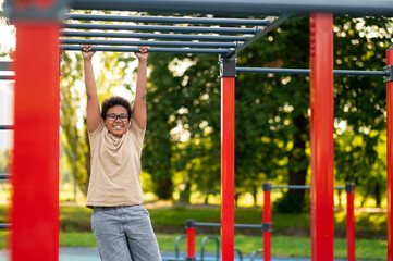 Obraz premium Curly-haired boy doing exercises at the playground in the morning