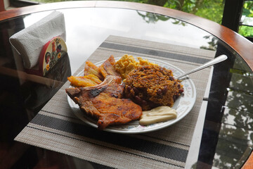 A top view of a plate of delicious Gallo pinto and pork chop with plantain, scrambled egg, and custard on a wooden table, a typical dish of Costa Rica.