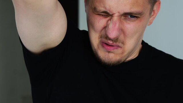 Smelly armpits due to sweat in a man.
The man does not take care of cleanliness and hygiene and an unpleasant smell comes from him.
A man with raised hands sniffs his armpits.