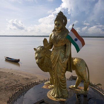 Aerial view of golden Bharat Mata statue standing proudly with the Indian flag near the riverbank, Assam, India.