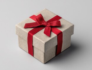 Obraz premium A square gift box, light beige color, adorned with a red ribbon and bow, sits on a plain gray background