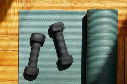 Overhead view of partially rolled yoga mat and weights on wooden floor