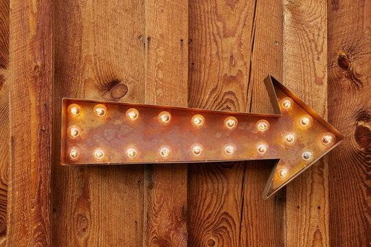 Illuminated arrow sign on wood background