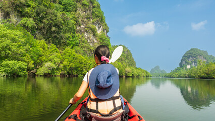 Woman in hat kayaking on river surrounded by trees and nature.