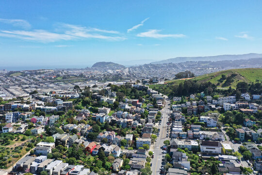 Aerial view of rows of houses and streets stretching out towards the distant hills and the ocean, a vibrant tableau under a bright sky., San Francisco, California, United States.
