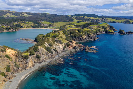 Aerial view of the rugged coastline meeting the turquoise sea, with green hills rolling into the horizon, Mahinepua Bay, Te Tai-tokerau, New Zealand.