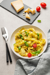 Tortellini pasta with parmesan, pesto and basil in a plate on a light  background with tomato, cheese and cutlery.