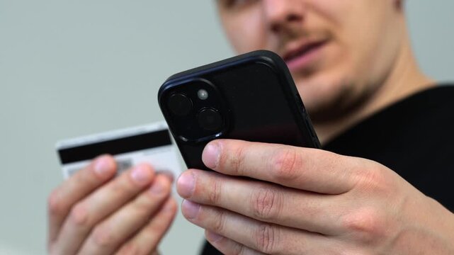 Online order and payment for goods using a credit card with money.
Money savings on a bank card of a man.
A guy with a mobile phone enters pinko d from a card