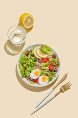 Flat lay of tuna salad with cherry tomatoes, eggs, olives and cucumbers in a plate on a bright yellow background