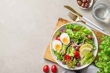 Tuna salad with olives, lettuce, tomatoes, eggs and lemon in a plate on a wooden board on a light background