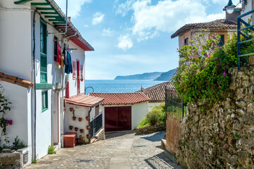 Sunny coastal village street with sea view, white houses, red roofs, and vibrant Mediterranean charm. Beautiful Spanish coastal town with traditional white houses and stunning ocean views. 