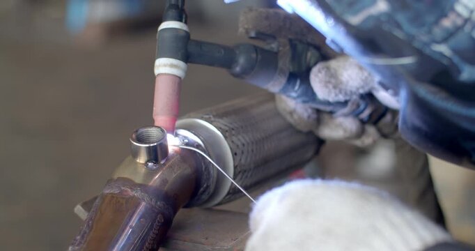 Technician is welding pipe to add position of o2 sensor.Car pipe welding.The hand of a mechanic or welder is fixing a car exhaust system.Tig welding makes the welds come out beautiful.