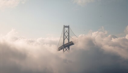 A tall suspension bridge tower rises above thick morning clouds, partially hidden within mist featuring soft sunlight illuminating the sky, creating the dreamy and atmospheric scene