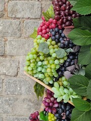 Autumn harvest display featuring colorful artificial grapes and leaves on a rustic stone background. Perfect for seasonal decor or winery themes, with copy space on the left.