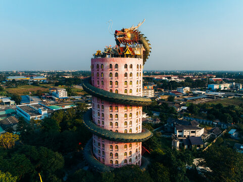 Aerial view of the vibrant pink Wat Samphran temple, a colossal dragon sculpture spiraling around its tower against the backdrop of lush greenery, Wat Sam Phran, Bangkok, Thailand.