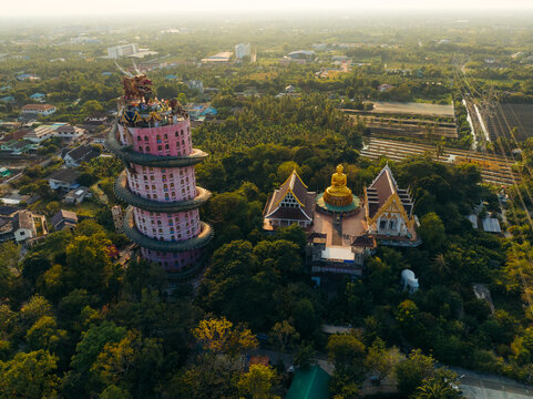 Aerial view of the striking pink tower and golden temple amidst lush greenery, a spiritual haven bathed in soft light, Wat Sam Phran, Bangkok, Thailand.