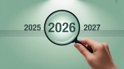 Conceptual image with years 2025, 2026, 2027 in a row on pastel green background. A hand holds a magnifying glass over 2026, enlarging it to symbolize focus, planning, and reflection