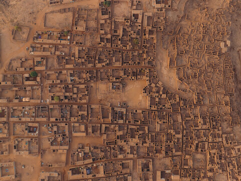 Aerial view of ancient structures and dwellings blend seamlessly with the arid landscape, creating a tapestry of ochre hues and textures, Ouadane, Adrar, Mauritania.