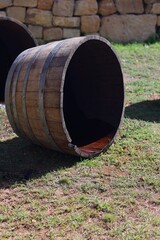 An empty wooden wine barrel lies on the grass near a stone wall, symbolizing tradition, craftsmanship, and the aging process of fine wines