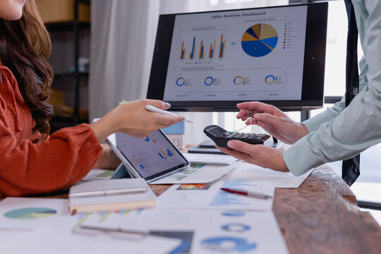 Business colleagues discussing sales analysis dashboard on computer screen while working together with calculator and digital tablet, analyzing financial data and planning strategy
