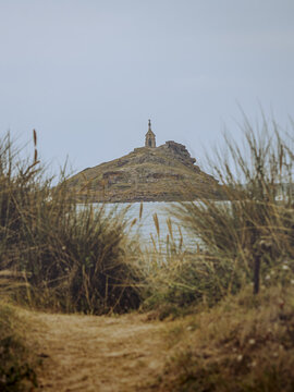 View of a rocky islet crowned with a monument, framed by golden grasses under a soft sky, inviting exploration and reflection, ilot Saint-Michel, Bretagne, France.