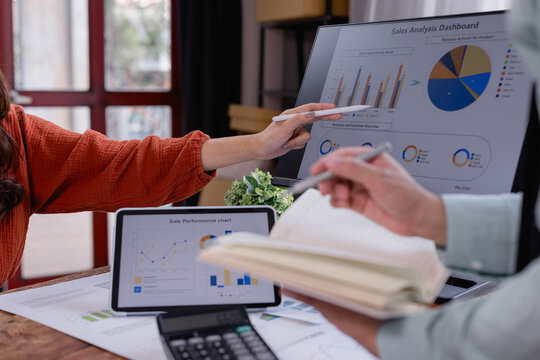 Marketing team working together analyzing sales performance dashboard on computer and tablet, taking notes and planning next strategy using data visualization and digital marketing