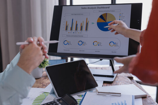 Marketing team analyzing sales data on a computer screen and discussing strategy in a modern office, using a digital pen to highlight charts and graphs