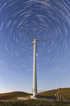View of a solitary wind turbine standing tall against a mesmerizing vortex of star trails in the clear night sky, Sommeralm, Styria, Austria.