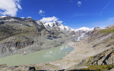 View of glacial watersof the melting Pasterze glacier, reflecting the sky, nestled amidst rocky mountains and snow-capped peaks under a vibrant blue sky, GroÃŸglockner, Carinthia, Austria
