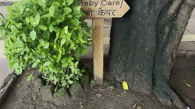 A wooden direction signboard showing directions for Toilet, Drinking Water, and Baby Care in both English and Hindi at a public place.