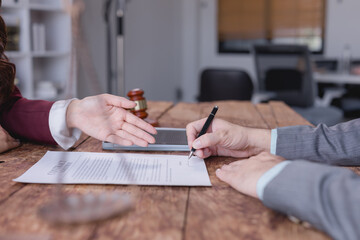 Businessman signing a contract after a successful negotiation with a lawyer, both seated at a wooden desk in a professional office environment, finalizing their agreement