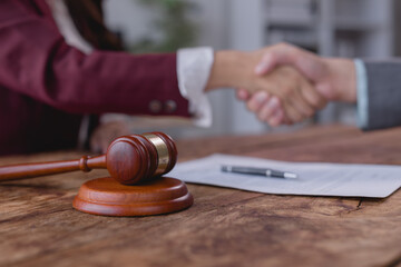 Two lawyers are shaking hands after signing a contract on a wooden table, with a gavel and a pen in...