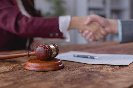 Two lawyers are shaking hands after signing a contract on a wooden table, with a gavel and a pen in the foreground, symbolizing legal agreement and justice